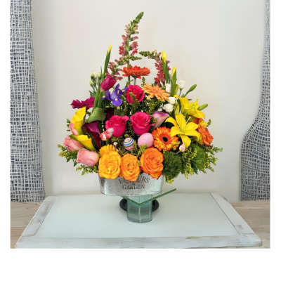 Colorful mixed flower arrangement with roses, lilies and gerberas in a metal container on a glass stand