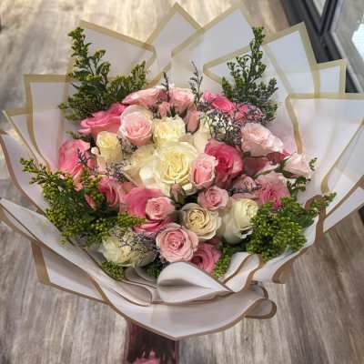 Hand-tied bouquet of pink and ivory roses wrapped in white paper with gold edging
