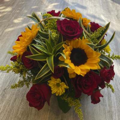 Round arrangement of yellow sunflowers and dark red roses with variegated foliage