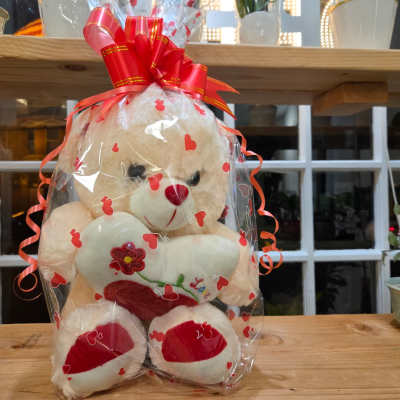 Cream teddy bear in heart-print cellophane with a red bow