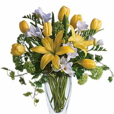 Yellow tulips and lilies in a clear glass vase with small white flowers