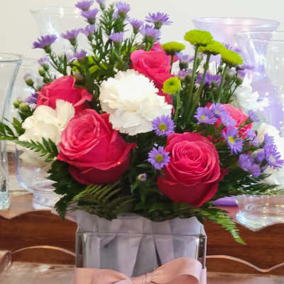 Pink roses and white carnations in a square glass vase with a pink ribbon
