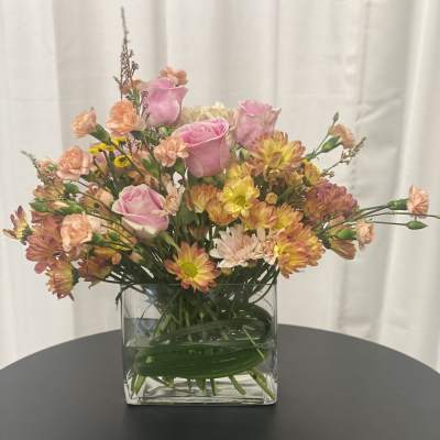 Pink roses and mixed blooms in a clear square vase