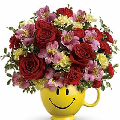 Red roses and pink flowers in a yellow smiley-face mug