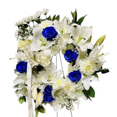 Standing wreath of white lilies and bright blue roses on a metal easel with white ribbon