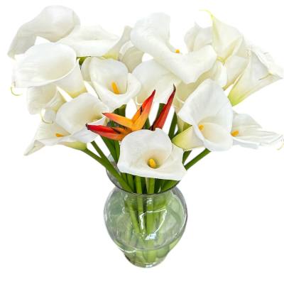 Tall arrangement of white calla lilies with orange tropical flowers in a clear glass vase