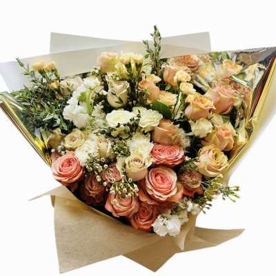 Bouquet of peach and cream roses with white flowers wrapped in gold and kraft paper