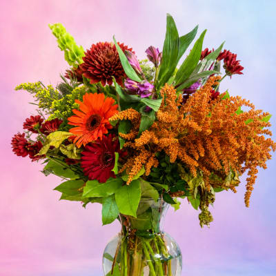 Mixed bouquet of orange, red, and purple flowers in a clear glass vase