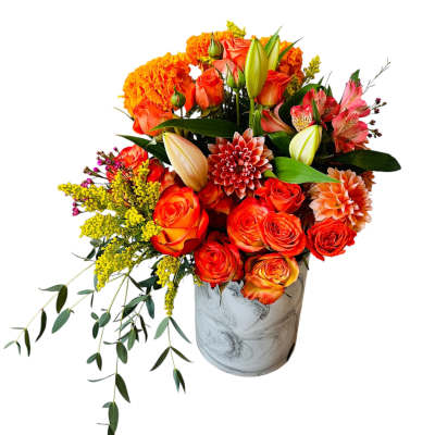 Asymmetrical orange and yellow flower arrangement with roses, lilies, and dahlias in a marbled white vase