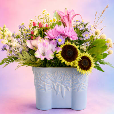 Mixed bouquet in a light blue ceramic vase with pink, yellow, and purple flowers