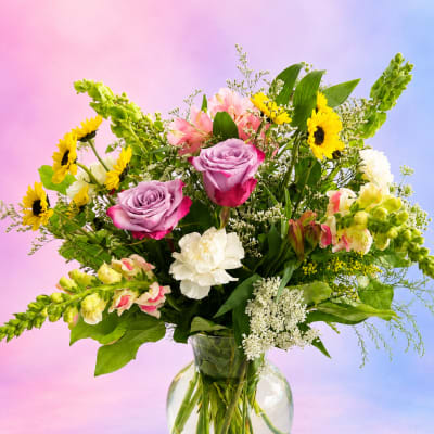 Mixed bouquet of roses, sunflowers, and lilies in a glass vase