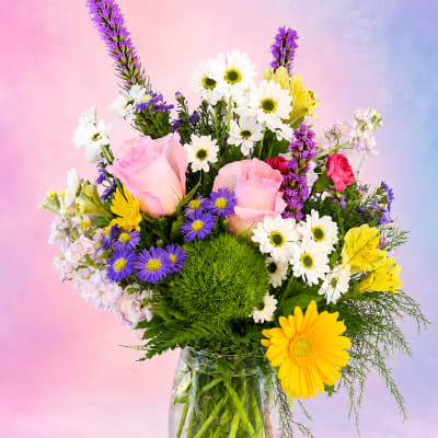 Mixed bouquet of pink roses, daisies, and purple flowers in a glass vase