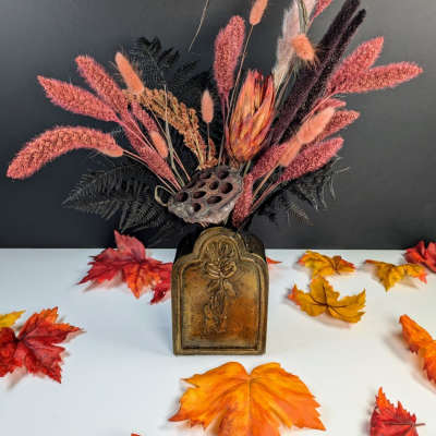 Dried floral arrangement in a decorative vase with autumn leaves