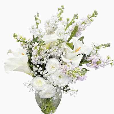 White and pale lavender flower arrangement with calla lilies and ranunculus in a clear glass vase