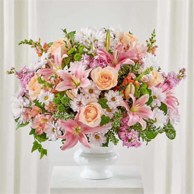 Pink lilies, peach roses, and white daisies in a white pedestal vase