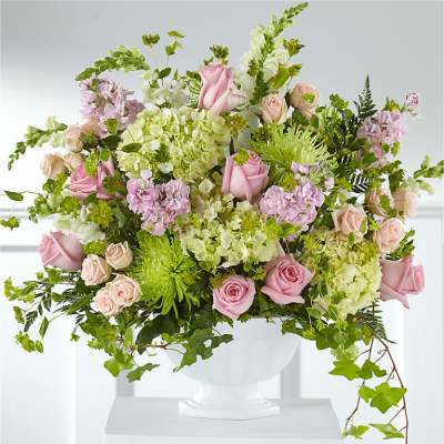 Pink roses and pale green hydrangeas in a white pedestal vase