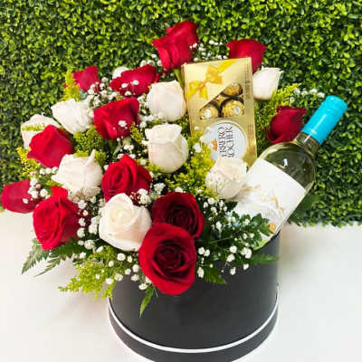 Red and white roses arranged in a black hat box with wine and chocolates