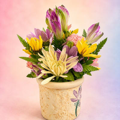 Mixed bouquet of purple, yellow, and cream flowers in a ceramic pot
