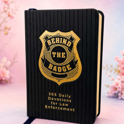 Black devotional book with gold badge emblem on a pink floral background.