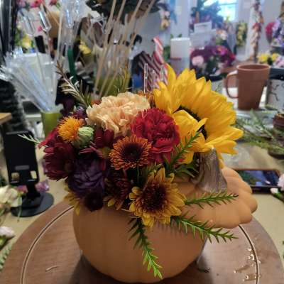Fall floral arrangement in a pumpkin-shaped container with sunflowers and mums