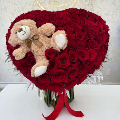 Heart-shaped red rose arrangement with a teddy bear and red ribbon