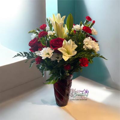 Bouquet of red roses, white lilies, and white daisies in a burgundy vase