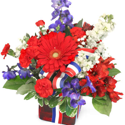 Red, white, and blue floral arrangement in a red glass vase with ribbon