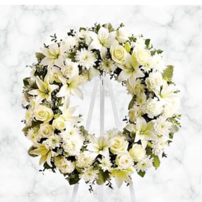 White floral wreath on a stand with roses and lilies
