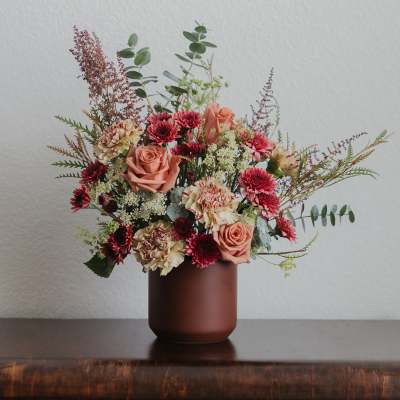 Mixed bouquet of peach roses and burgundy flowers in a brown vase