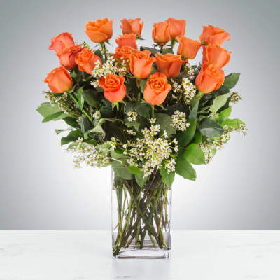 Tall arrangement of orange roses with small white blooms in a clear glass vase