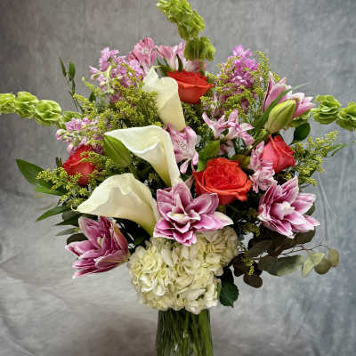 Mixed bouquet with pink lilies, red roses, white calla lilies, and hydrangea in a glass vase