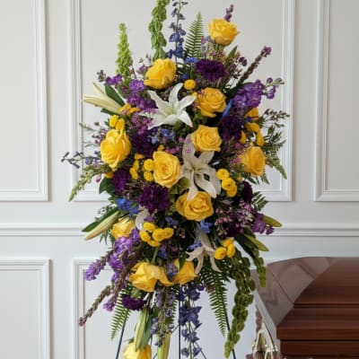 Tall funeral spray with yellow roses, white lilies, and purple flowers on a stand