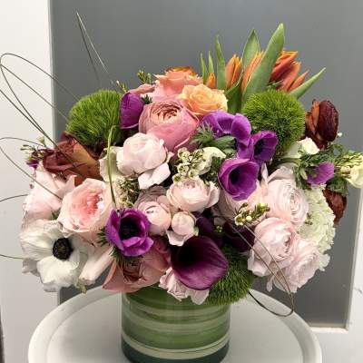 Mixed pink, purple, and orange flowers arranged in a green glass vase.