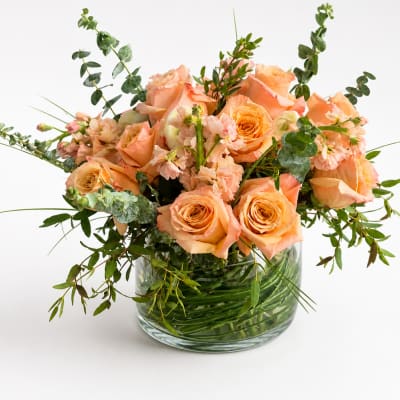 Peach roses and small pink flowers in a clear glass vase