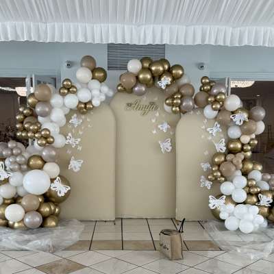 Gold, white, and beige balloon arch around a backdrop with butterfly decorations