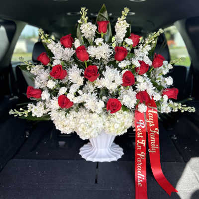 Red roses and white flowers arranged in a white vase with a red ribbon