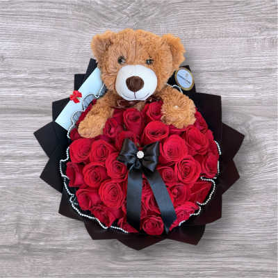 Teddy bear sitting on a bouquet of red roses with a black ribbon