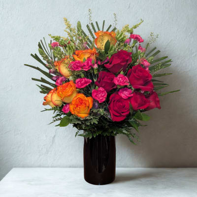 Bouquet of orange and red roses in a dark vase