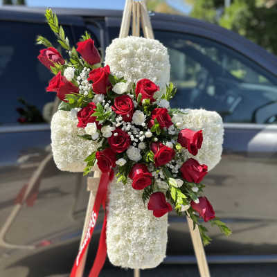 Red roses arranged on a white floral cross on an easel