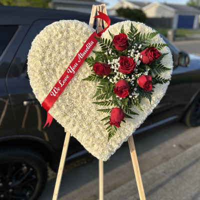 Heart-shaped white floral tribute with red roses on an easel