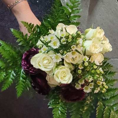 Handheld bouquet of white roses and small white daisies with dark purple blooms