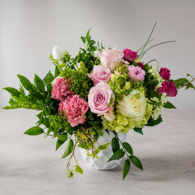 Mixed pink, white, and green floral arrangement in a white vase