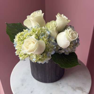 Cream roses and pale hydrangeas in a dark round vase
