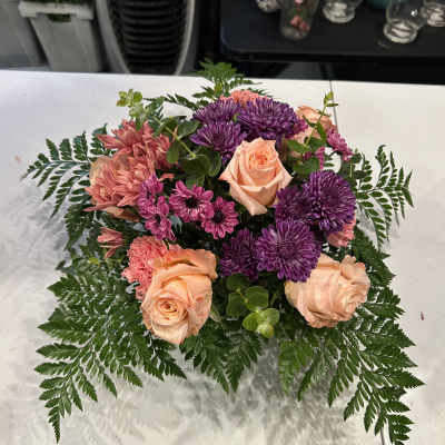 Peach roses and purple chrysanthemums in a low floral arrangement