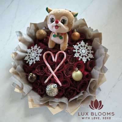 Bouquet of red roses with a plush reindeer and holiday ornaments