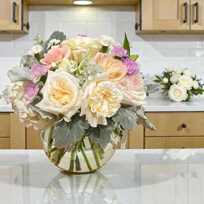 Bouquet of cream, blush, and lavender flowers in a clear glass vase