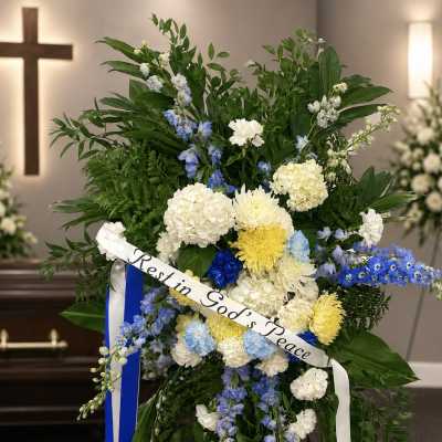 Standing sympathy spray with white, blue, and yellow flowers and a "Rest in God's Peace" ribbon