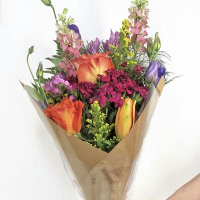 Mixed bouquet of orange, pink, purple, and yellow flowers wrapped in brown paper