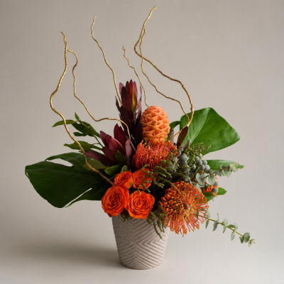 Orange and burgundy tropical flowers in a textured vase