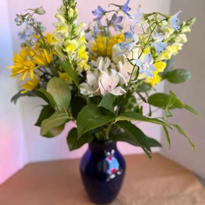 Mixed bouquet of yellow, blue, and pale pink flowers in a dark vase
